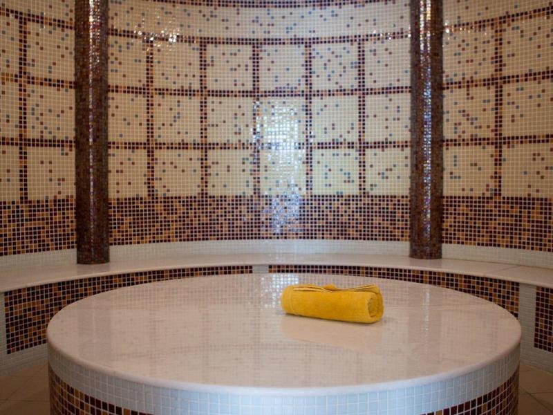 Mesa redonda de mosaico con toalla clara en una sala de baño de vapor decorativa y circular.