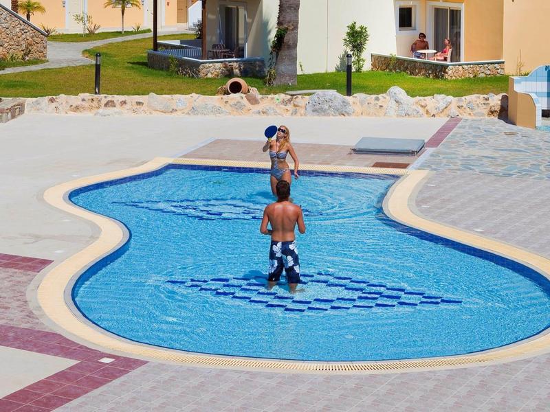 Niños jugando en la piscina exterior poco profunda de forma curva de un hotel bajo el sol.