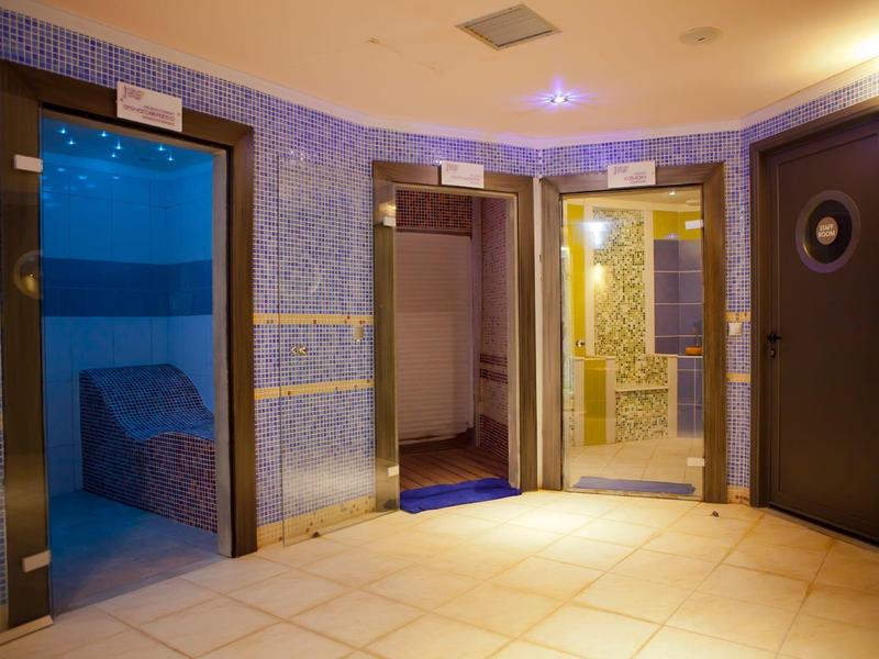 Zona interior con tres puertas, pasillo iluminado y paredes de mosaico azul en área de spa.