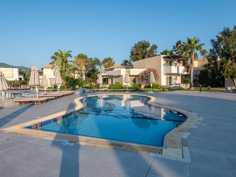 Piscina moderna de hotel con tumbonas y palmeras bajo cielo despejado.
