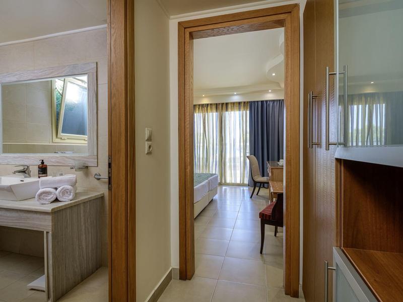 Vista a través del pasillo a la habitación del hotel con baño a la izquierda y cortina en la ventana al fondo.