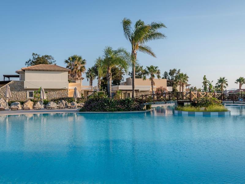 Gran piscina exterior con palmeras y tumbonas en un hotel bajo un cielo despejado.