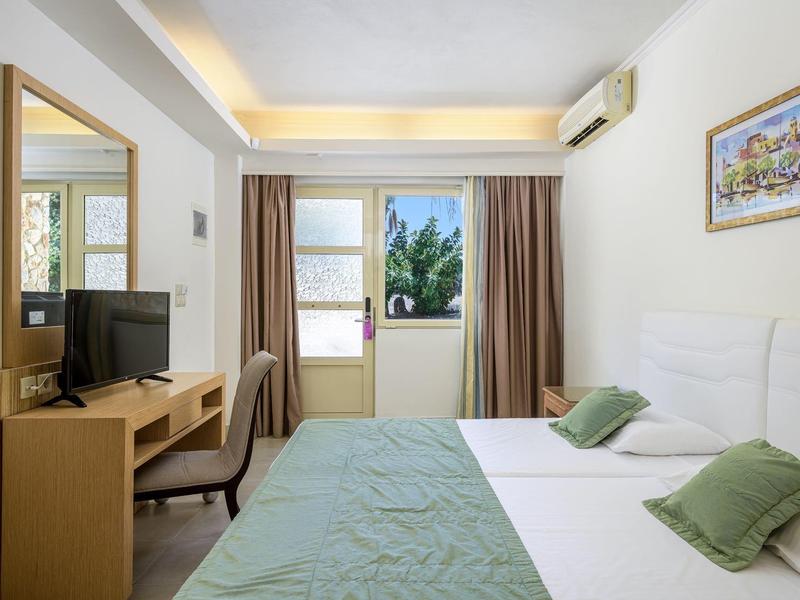 Habitación de hotel luminosa con cama doble, escritorio, televisor y ventana con vista a árboles.