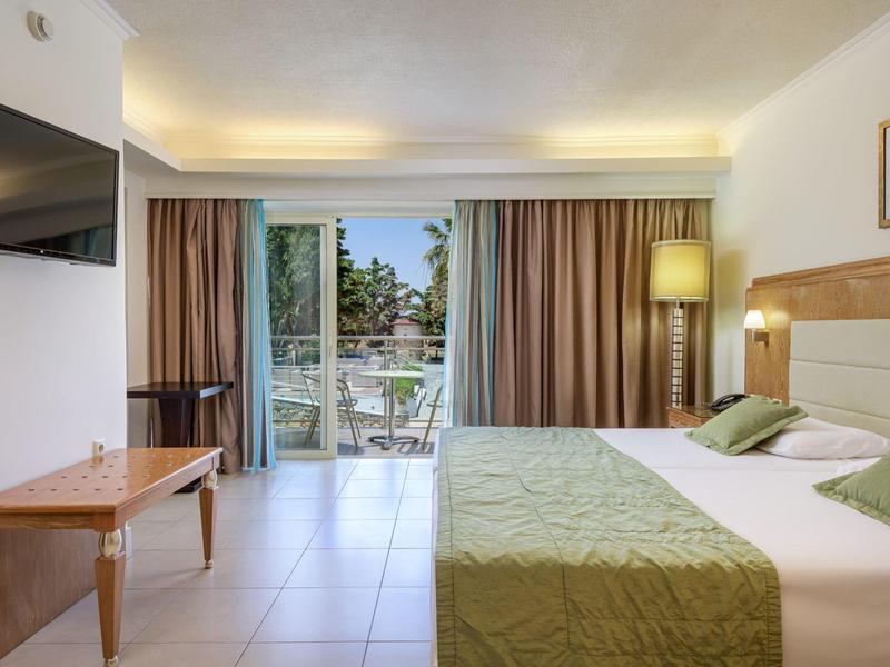 Habitación de hotel luminosa con cama doble y terraza con vistas a palmeras.