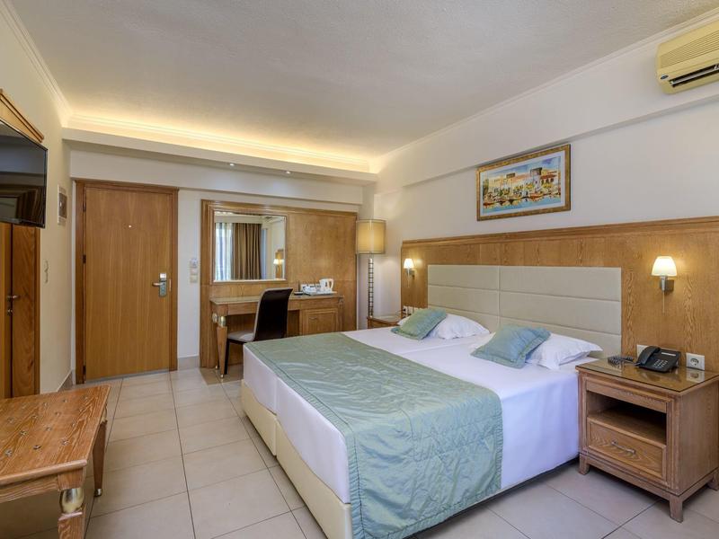 Habitación de hotel luminosa con cama grande, escritorio, TV e iluminación elegante.