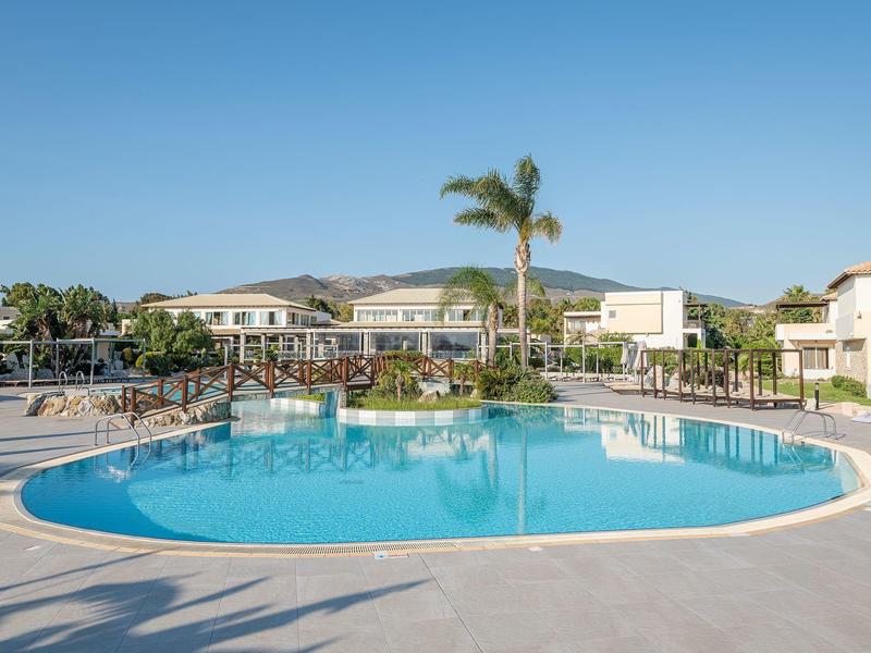 Piscina redonda al aire libre con palmeras y edificios blancos en un complejo turístico soleado.