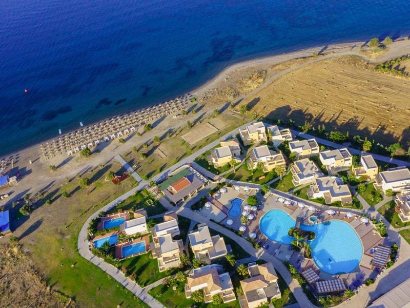 Vista aérea de un resort en la playa con piscinas y sombrillas junto al mar.