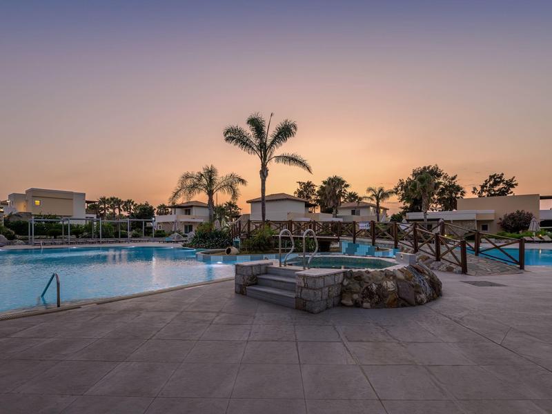 Área de piscina del hotel al atardecer con palmeras y zonas de descanso al aire libre.