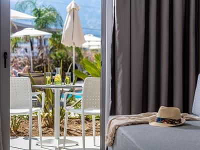 Vista attraverso porta finestra aperta su terrazza con tavolo, sedie e ombrellone accanto a un divano grigio.