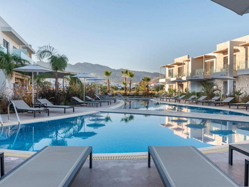 Nowoczesny hotelowy basen z leżakami i górskim tłem o zachodzie słońca.