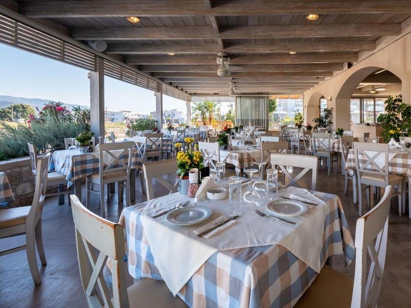 Jasna część restauracyjna z nakrytymi stolikami i widokiem na krajobraz śródziemnomorski.