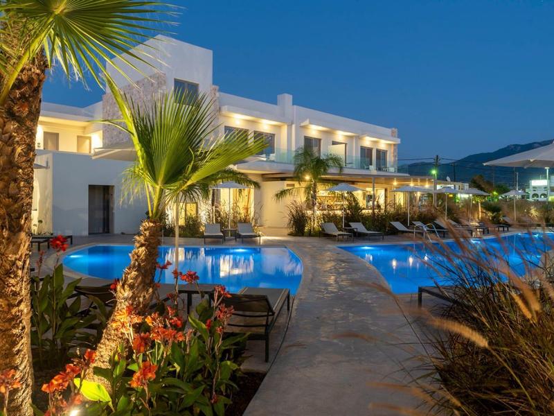 Oświetlony hotel z basenem i palmami o zmierzchu