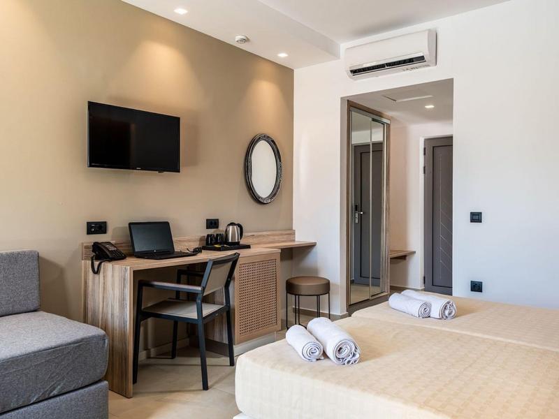 Nowoczesny pokój hotelowy z dwoma łóżkami, biurkiem, krzesłem i telewizorem na ścianie.