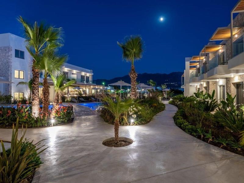 Nowoczesny kompleks hotelowy z oświetlonymi ścieżkami i palmami nocą pod czystym niebem.