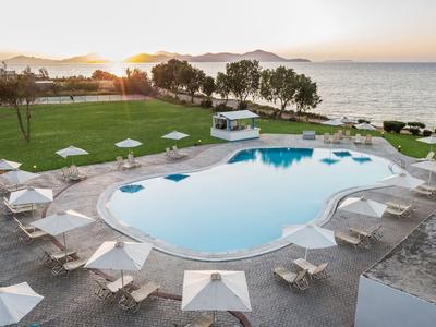 Una piscina con ombrelloni bianchi e sdraio vicino al mare al tramonto.
