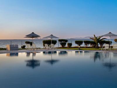 Zona piscina tranquilla con lettini e ombrelloni vicino al mare al tramonto.