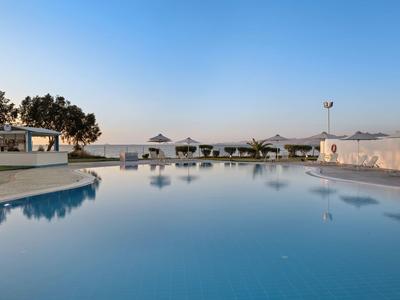 Piscina all'aperto calma con lettini e ombrelloni al tramonto, cielo limpido riflesso nell'acqua.