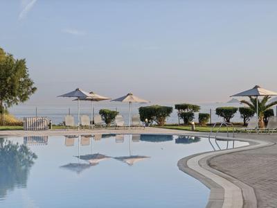 Piscina con ombrelloni e posti a sedere, vista sul mare sotto un cielo sereno