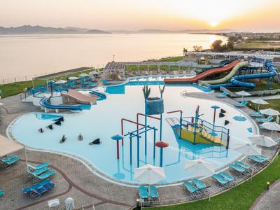 Grande piscina esterna con scivoli d'acqua e area giochi acquatica, circondata da lettini vicino al mare.
