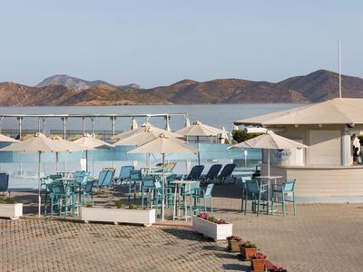Area esterna con sedie blu e ombrelloni vicino a un padiglione bianco e colline.
