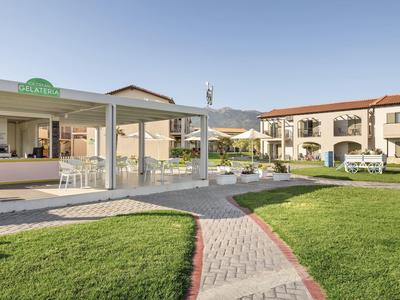 Area esterna con prato verde, sentiero, struttura aperta e edificio dell'hotel a due piani