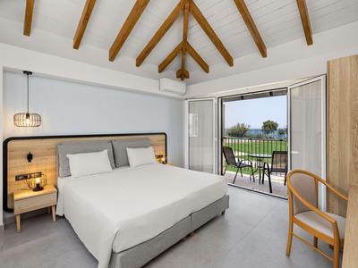 Camera d'hotel luminosa con letto matrimoniale, soffitto in legno e balcone con vista sull'area verde.