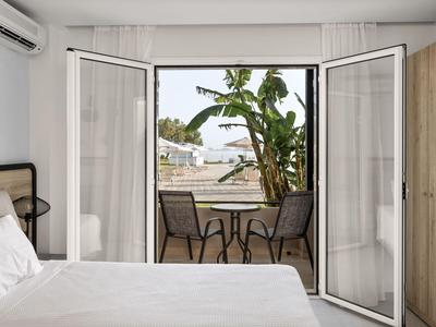 Camera d'hotel con porte doppie aperte che conducono a una terrazza con sedie, tavolo e vista sulle palme.