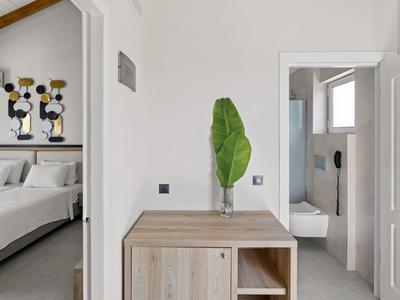 Corridoio di hotel moderno con mobile in legno, grande foglia verde e vista su camera e bagno.