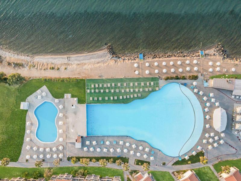 Una grande piscina all'aperto e una piscina più piccola sul mare con lettini e ombrelloni.