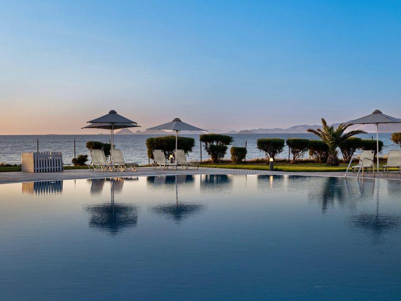 Scena tranquilla a bordo piscina con ombrelloni e lettini vicino al mare al tramonto.