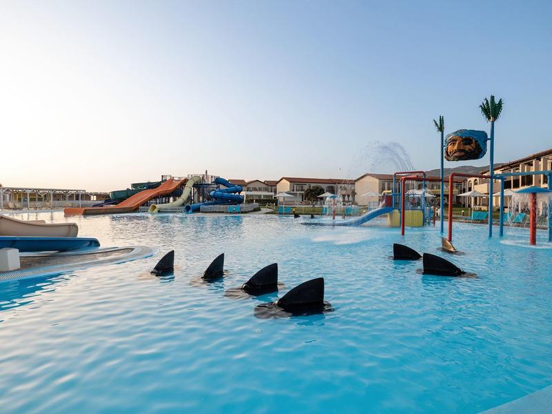 Piscina per bambini con varie strutture ludiche acquatiche e scivoli in un resort.