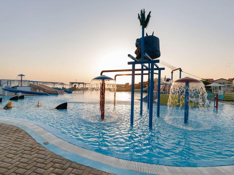 Area giochi acquatica all'aperto con scivoli e fontane al tramonto.