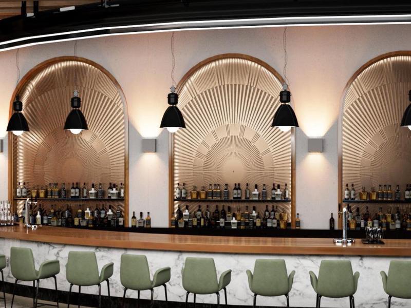 Bar moderno con sedie verdi e scaffali ad arco con bottiglie su una parete beige calda.