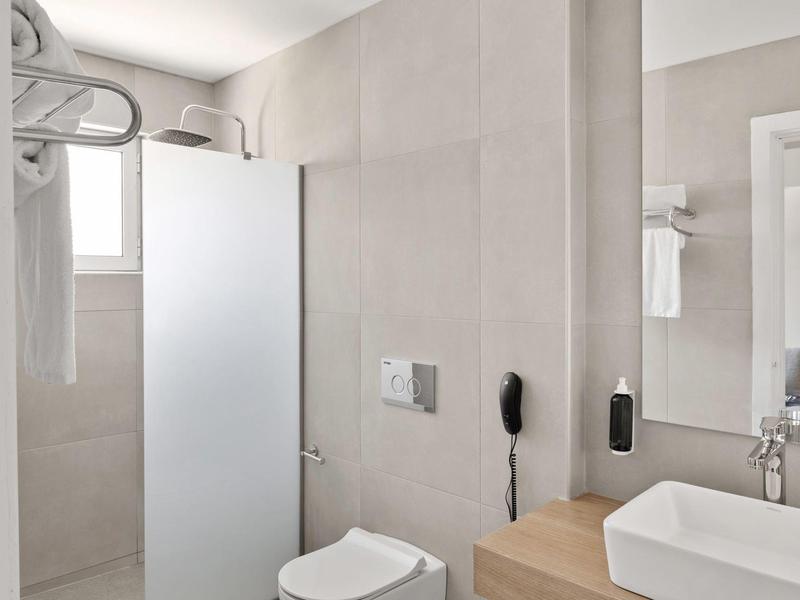 Bagno d'hotel moderno e luminoso con doccia, WC, lavabo e asciugamani.