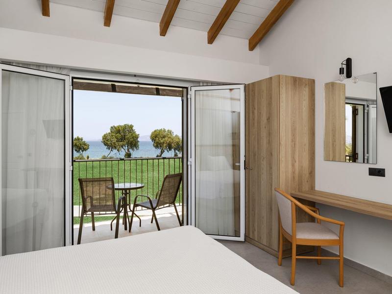 Camera d'hotel moderna con balcone che si affaccia su prato verde e alberi vicino al mare.