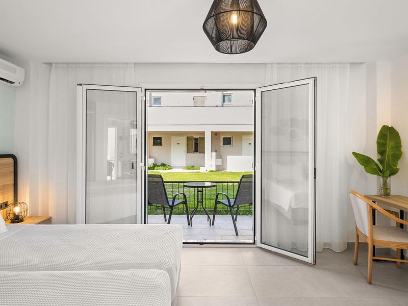 Camera d'albergo luminosa con letto, scrivania e porte aperte su balcone con tavolo e sedie.