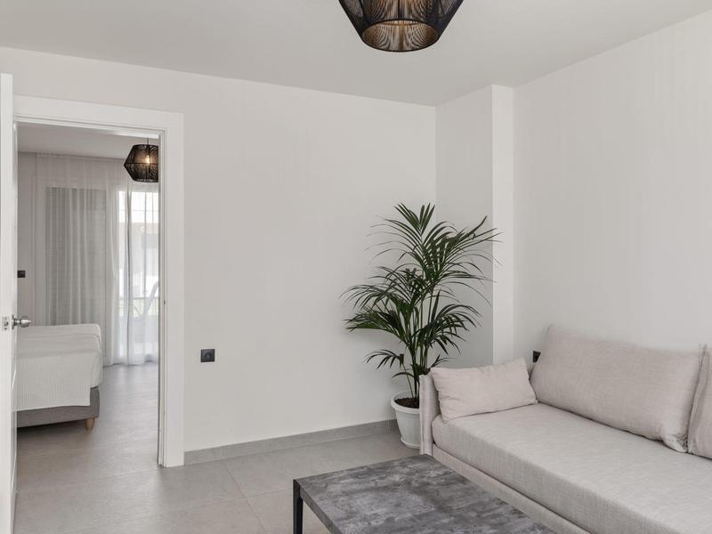 Camera d'hotel minimalista con divano grigio, tavolino nero e pianta in vaso.