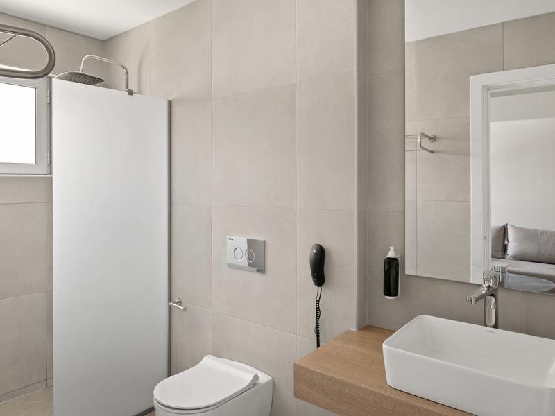Bagno moderno con wc bianco, lavabo rettangolare, grande specchio e piastrelle beige neutre.