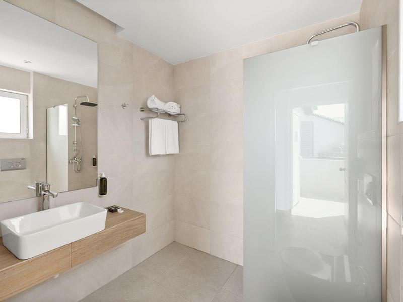 Bagno moderno in hotel con lavabo, grande specchio, asciugamani e box doccia in vetro.