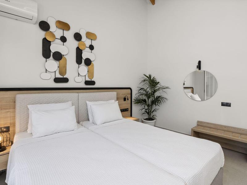 Camera d'hotel luminosa con due letti singoli, biancheria bianca, decorazioni murali, specchio rotondo e panca in legno.