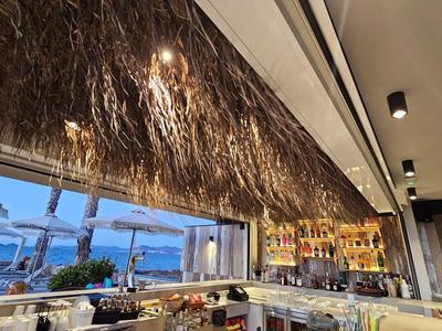 Area ristorante moderna con soffitto in paglia e vista sul mare al crepuscolo.