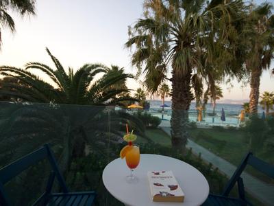 Tavolo con bevanda e libro su balcone con vista su palme e mare al tramonto.