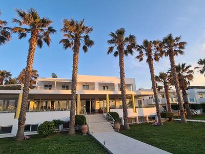 Modernes Hotelgebäude mit Palmen und gepflegtem Rasen bei Sonnenuntergang.