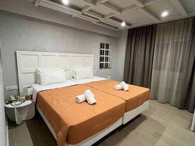 Moderní hotelový pokoj se dvěma jednolůžky, oranžovým povlečením a šedými závěsy.