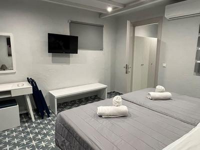 Moderní hotelový pokoj se dvěma postelemi, televizorem, psacím stolem a vzorovanou dlažbou.