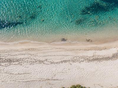 Luftaufnahme eines hellen Sandstrands neben klarem, türkisfarbenem Wasser.