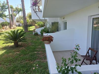 Ein Balkon mit zwei Holzstühlen und Pflanzen, mit Blick auf einen grünen Garten und Palmen.