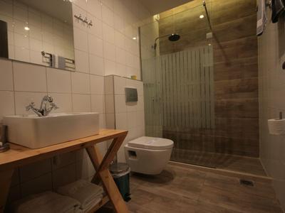 Modernes Badezimmer mit Dusche, Toilette und Waschbecken auf Holzablage in warmem Licht.