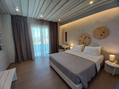 Modernes Hotelzimmer mit großem Bett, grauer Bettdecke, runden Holzdekorationen und Balkon.