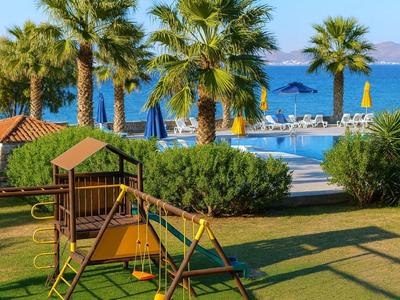 Hotelgarten mit Spielplatz, Palmen und Pool mit Meerblick im Hintergrund.